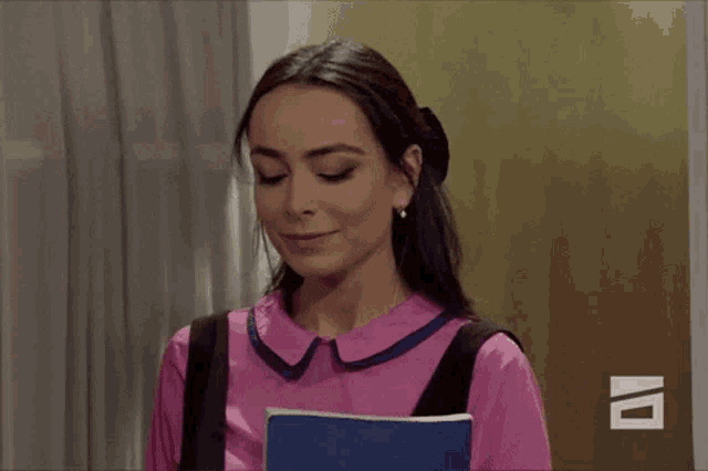 a woman in a pink shirt is smiling and holding a book