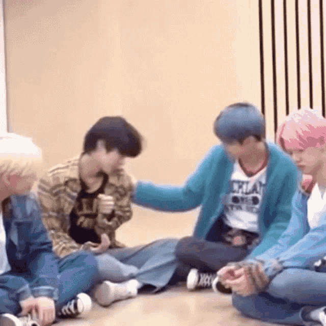 a group of young men are sitting on the floor and one of them is petting another man 's head .