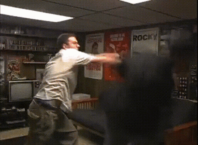 two men are fighting in a room with rocky posters on the wall behind them