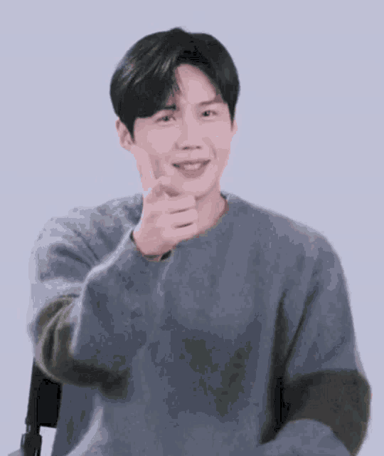 a young man in a grey sweater is giving a thumbs up sign .