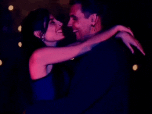 a man and a woman are dancing in a dark room with blue lights behind them