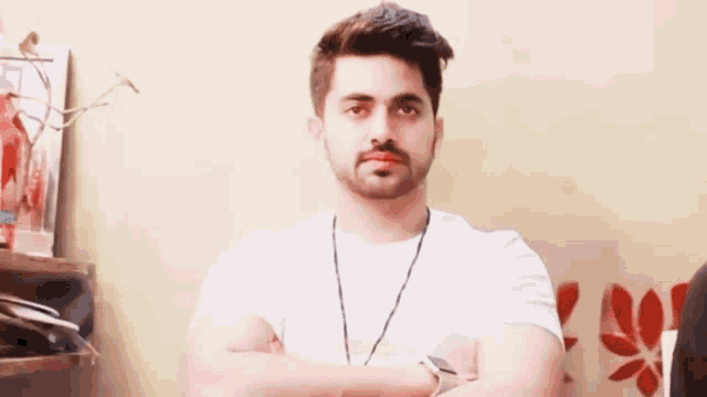 a man with a beard is standing with his arms crossed in front of a wall .