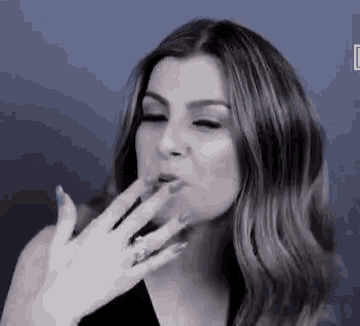a black and white photo of a woman blowing a kiss with her hand .