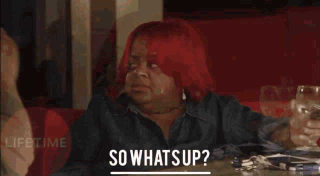 a woman with red hair is sitting at a table with a glass of wine and says " so whats up "