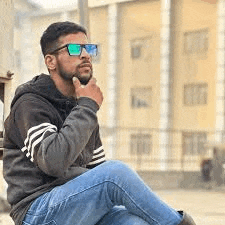 a man wearing sunglasses and a hoodie is sitting on the ground .