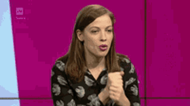 a woman is sitting in front of a pink wall and talking to someone