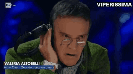 a man wearing glasses and a green jacket is talking into a microphone with the name valeria altobelli on the bottom