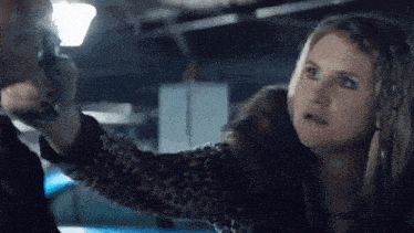 a woman is holding a gun to a man 's head in a dark room .