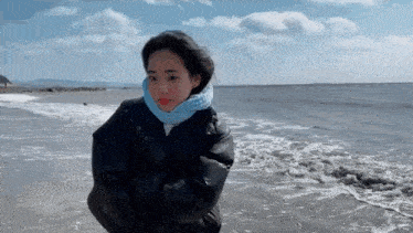 a woman wearing a scarf and a jacket is standing on the beach
