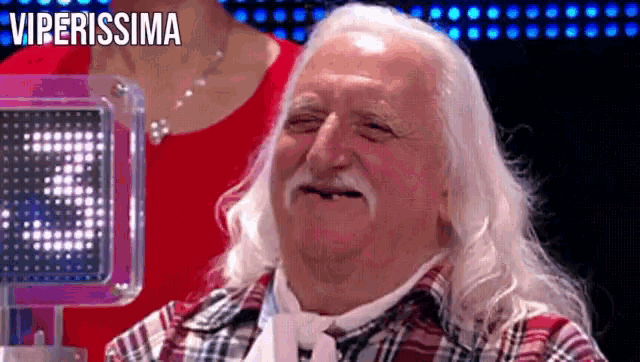 an older man with long white hair and a mustache is smiling in front of a screen that says viperissima