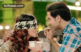 a man is feeding a blindfolded woman a bowl of food with a spoon .