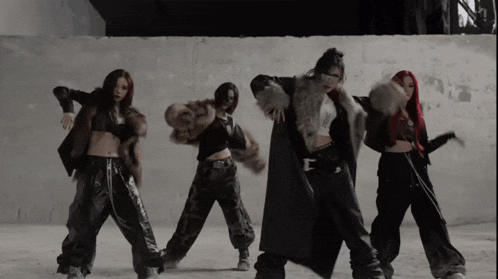 a group of women are dancing in front of a wall and one of them is wearing a fur coat