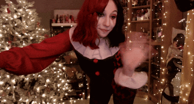 a woman in a red and black clown costume is dancing in front of a christmas tree