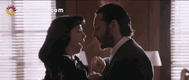a man and a woman are kissing in front of a screen that says eltrecetv.com on it