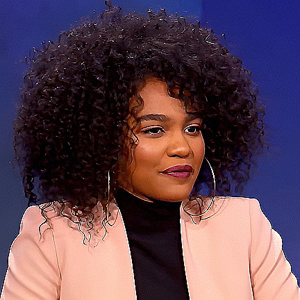 a woman with curly hair and hoop earrings is wearing a pink jacket