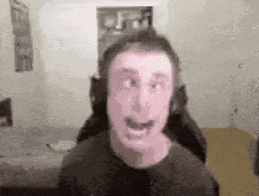 a man is wearing headphones and making a funny face while sitting in a chair .