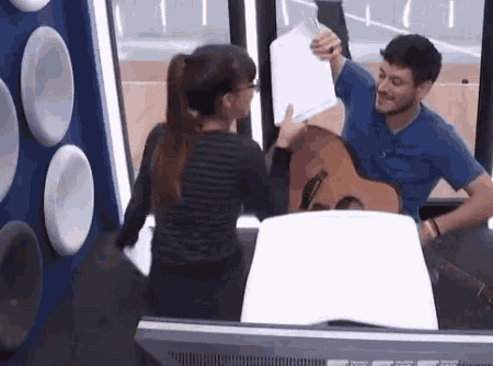 a man playing a guitar and a woman holding a piece of paper in front of a television .
