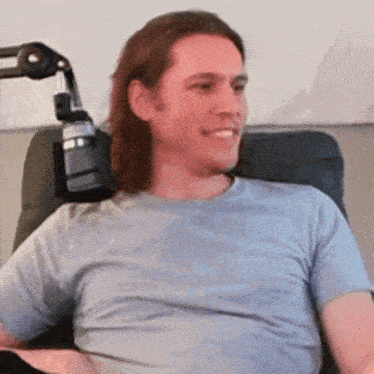 a man with long hair is sitting in a chair with a microphone attached to his arm