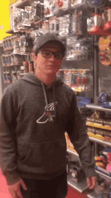 a man wearing a hat and glasses is standing in front of a shelf of toys