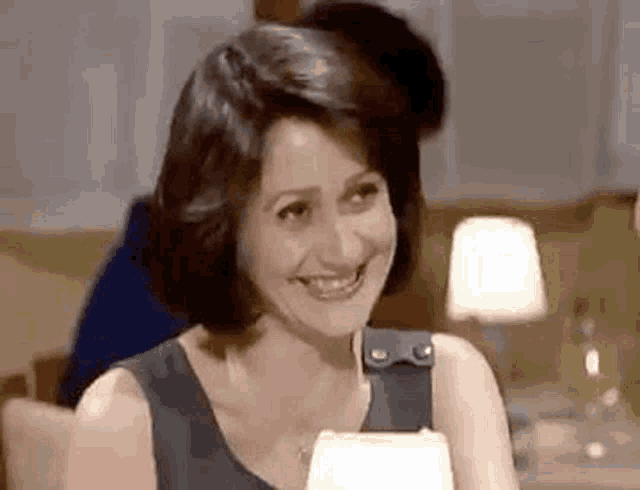 a woman is smiling while sitting at a table with a man behind her .