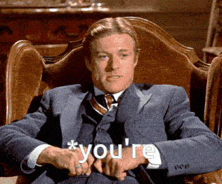 a man in a suit and tie sits in a chair with the words * you 're * on his arm