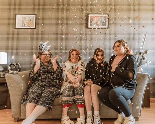 four women are sitting on a couch with confetti falling