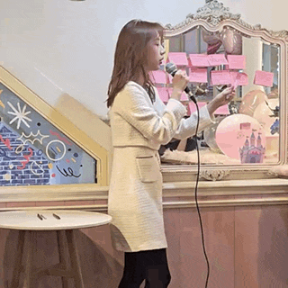 a woman is singing into a microphone in front of a mirror in a room .
