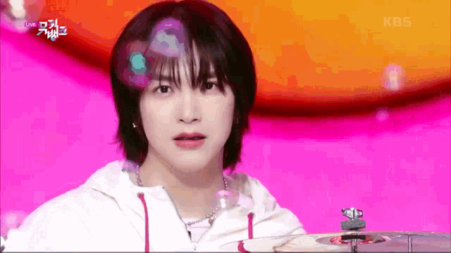 a young man with short hair is playing drums on a pink background