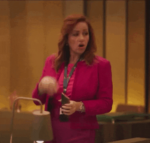a woman in a pink suit is holding a bottle of champagne and making a funny face .