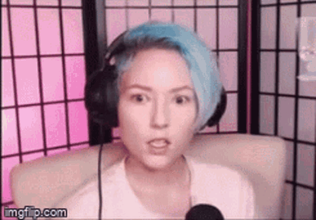 a woman with blue hair is sitting in front of a microphone wearing headphones and making a funny face .