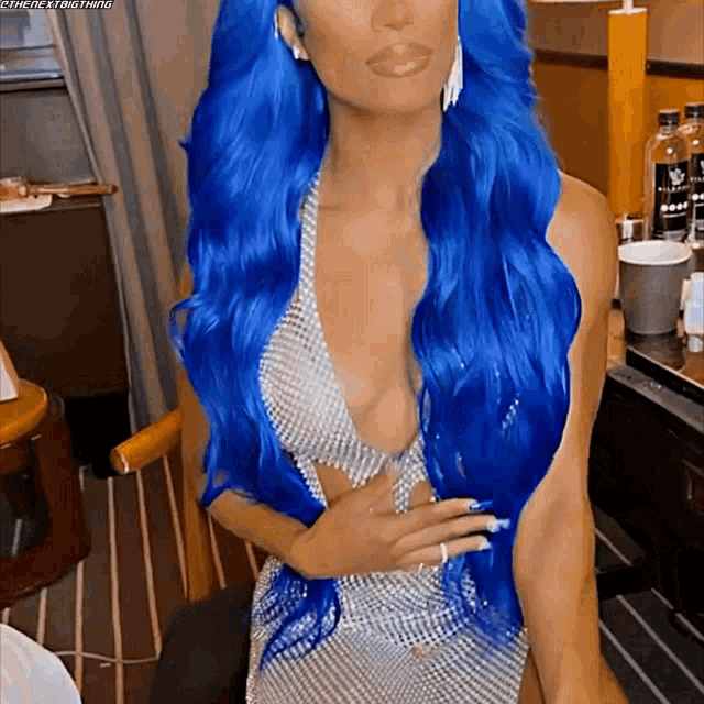 a woman with blue hair is wearing a plunging silver top