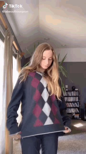 a woman is standing in a living room wearing a sweater that has a checkered pattern .