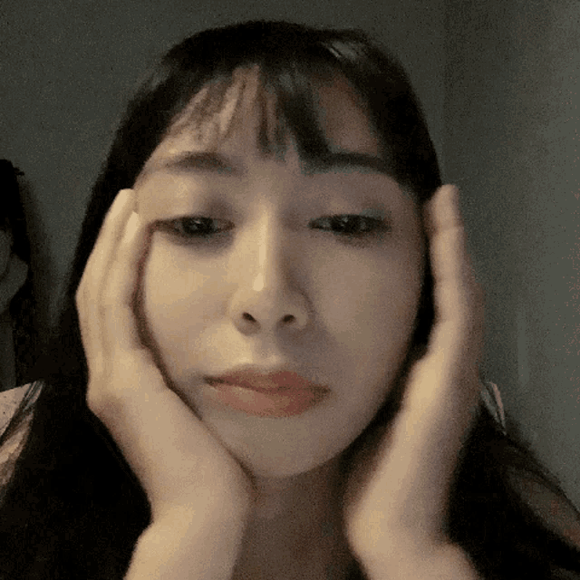 a woman holds her hands to her face and looks at the camera
