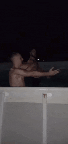 two men are standing in a pool at night .