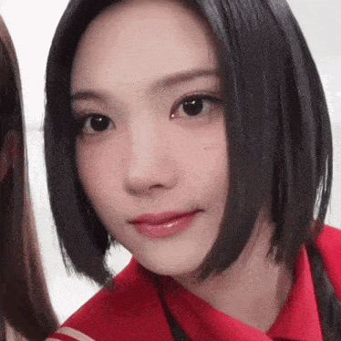 a woman with short black hair is wearing a red shirt and looking at the camera