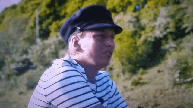 a man wearing a striped shirt and a hat is sitting in a field