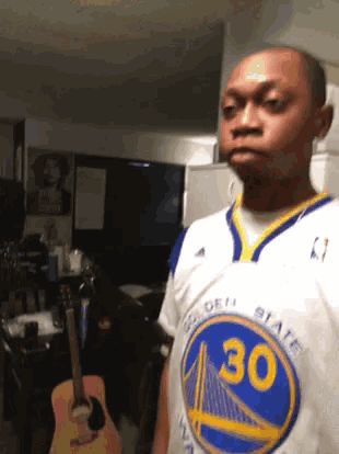 a man in a golden state warriors jersey stands in front of a guitar