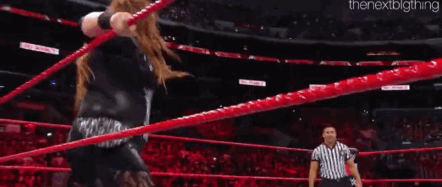 a woman is standing in a wrestling ring with a referee standing behind her .