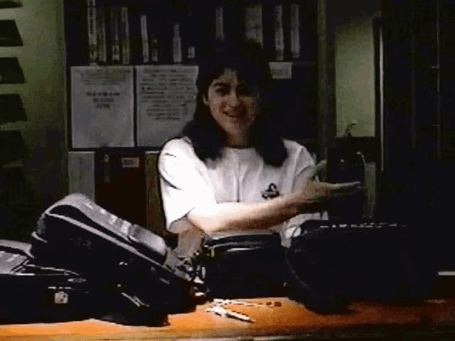 a woman in a white t-shirt with the letter s on it stands at a desk