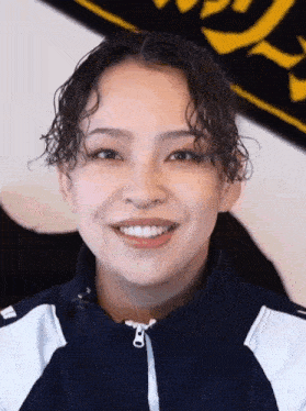 a woman with curly hair is smiling in front of a black and yellow banner .