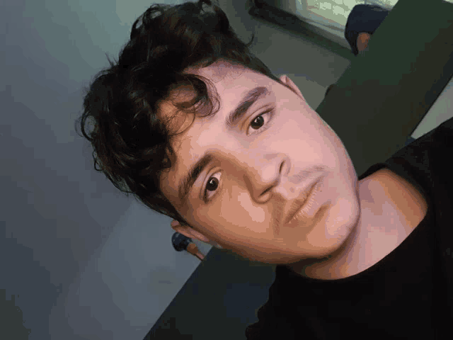 a young man with curly hair and a black shirt looks at the camera