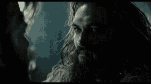 a close up of a man with long hair and a beard looking at another man .