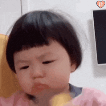 a baby girl with short hair is eating a banana and making a face .