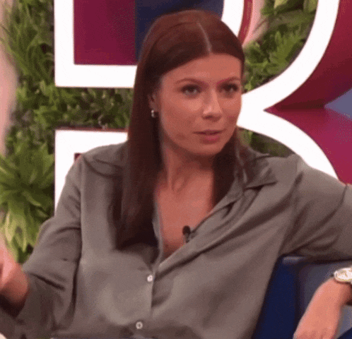 a woman wearing a grey shirt is sitting in front of a sign that says l
