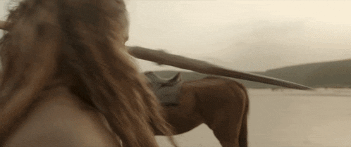 a woman is riding a horse in the desert and holding a spear .