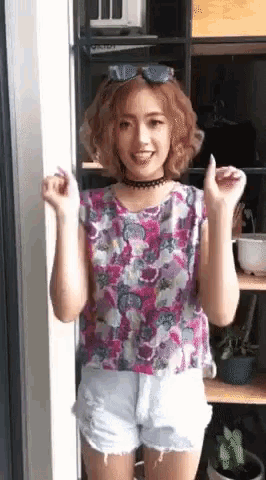 a woman in a floral top and white shorts is standing in front of a door .