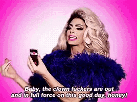 a drag queen is holding a cell phone and says baby the clown fuckers are out and in full force on this good day honey