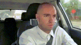 a bald man in a white shirt and tie is driving a car .