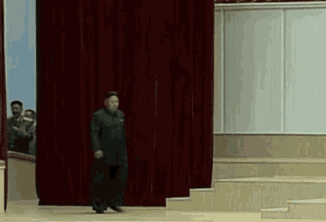 a man standing on a stage with a red curtain