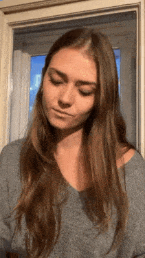 a woman with long hair is standing in front of a window and making a funny face .